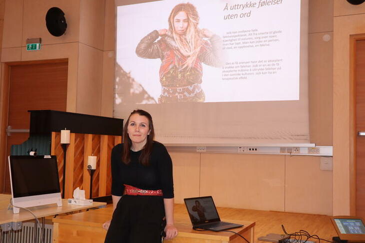 Terapeut ved Viken senter Mirja Päiviö sitter foran et bilde av en samisk kvinne med teksten Å uttrykke følelser uten ord