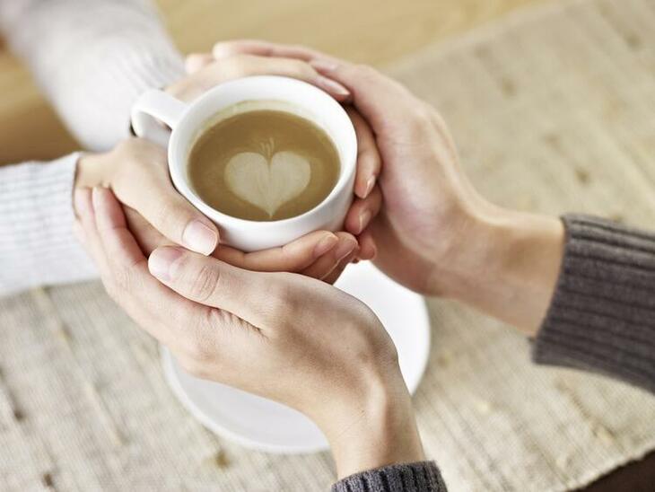 Et par holder om en kopp kaffe med hjerte i